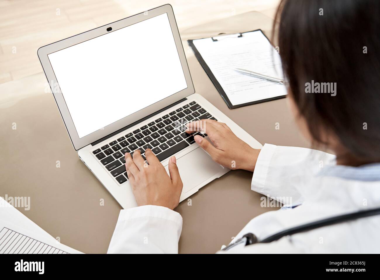 Dottore indiano che scrive usando il computer portatile mock up schermo bianco alla scrivania, primo piano. Foto Stock