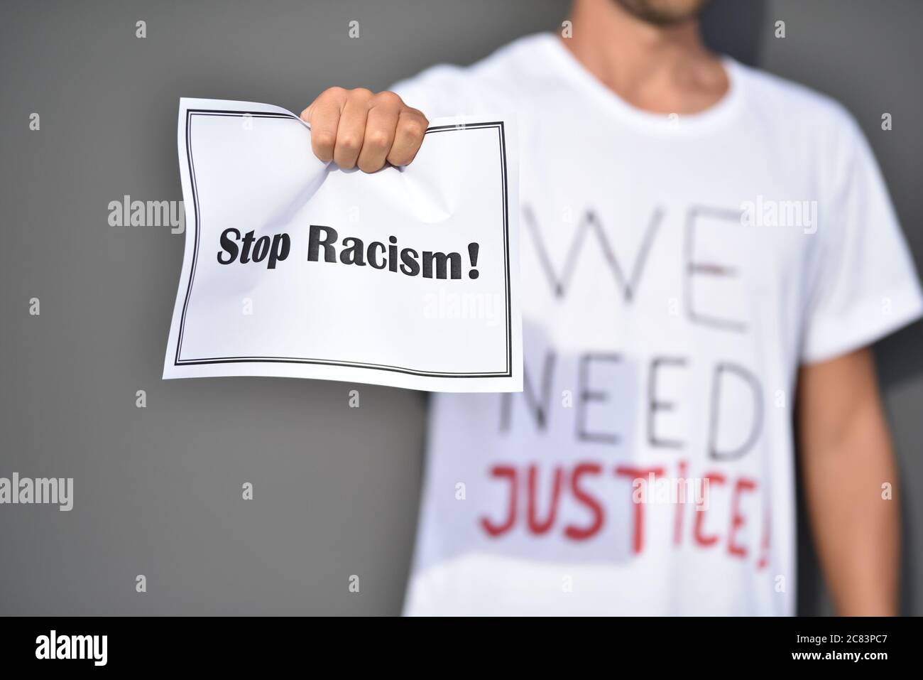 L'uomo tiene carta con parole Stop Racism davanti alla parete grigia. Le vite nere contano Foto Stock