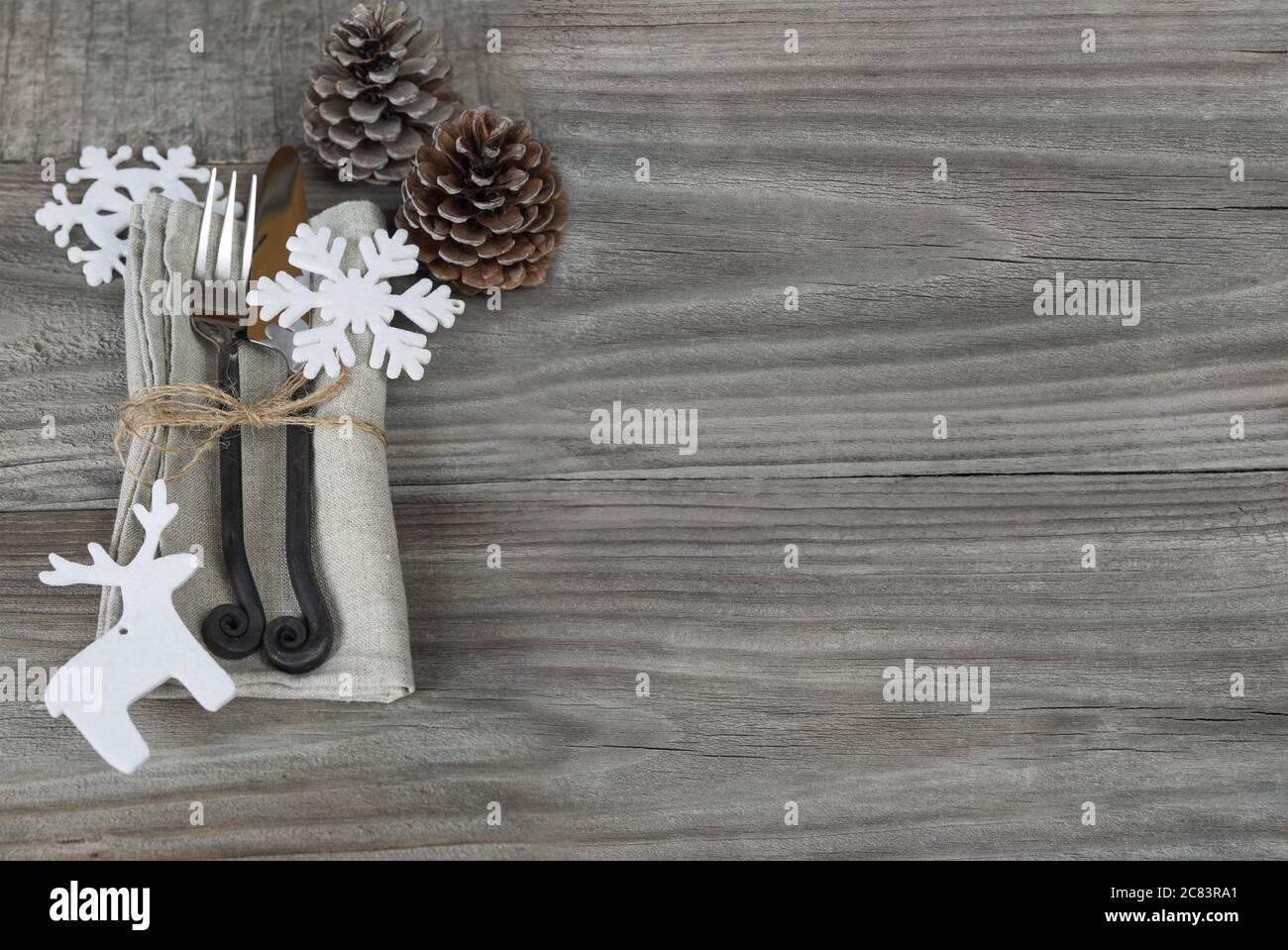 Forchetta in acciaio e coltello fatti a mano giacciono su un tovagliolo di lino legato con spago ruvido, nonché due coni di pino e un giocattolo in feltro bianco sotto forma di fiocco di neve e. Foto Stock