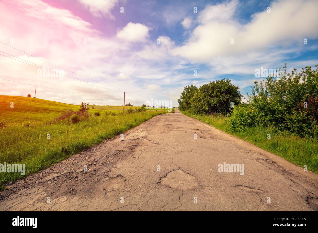 Vecchia strada di campagna in buche e buche. Paesaggio rurale in una giornata di sole. Foto Stock