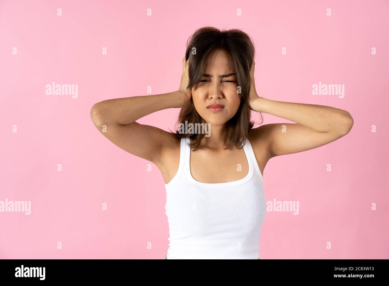 Giovane donna frustrata con gli occhi chiusi coprendo le orecchie con le mani su fondo rosa chiaro Foto Stock