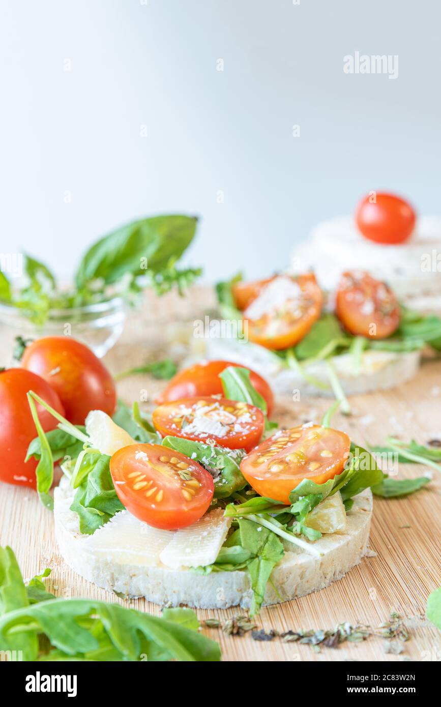 Angri, Italia. Immagine alimentare di cracker di riso spuntino con pomodori, insalata di razzi, fiocchi di parmisan, origano e olio d'oliva, su un tagliere di legno. Itali Foto Stock