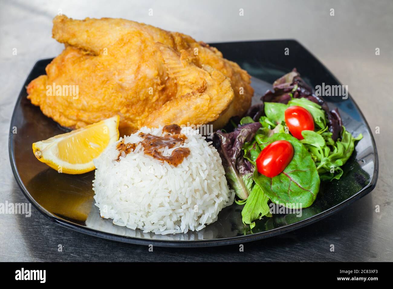 Un piatto di cibo occidentale consiste di un intero pollo primaverile, riso e insalate. Foto Stock