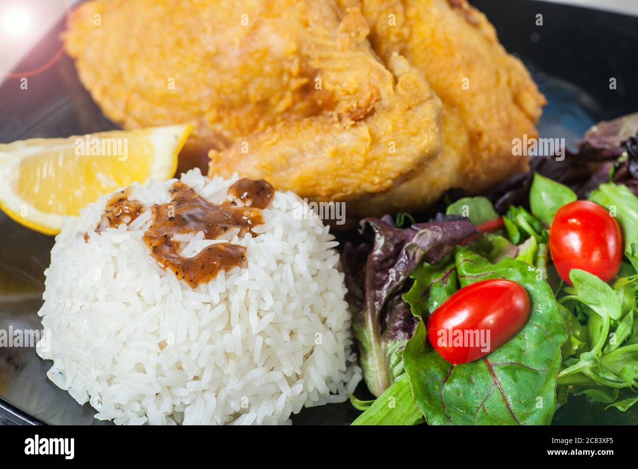 Primo piano di una piastra di riso, un intero pollo fritto e insalata, luce svasata in alto a sinistra come effetto. Foto Stock