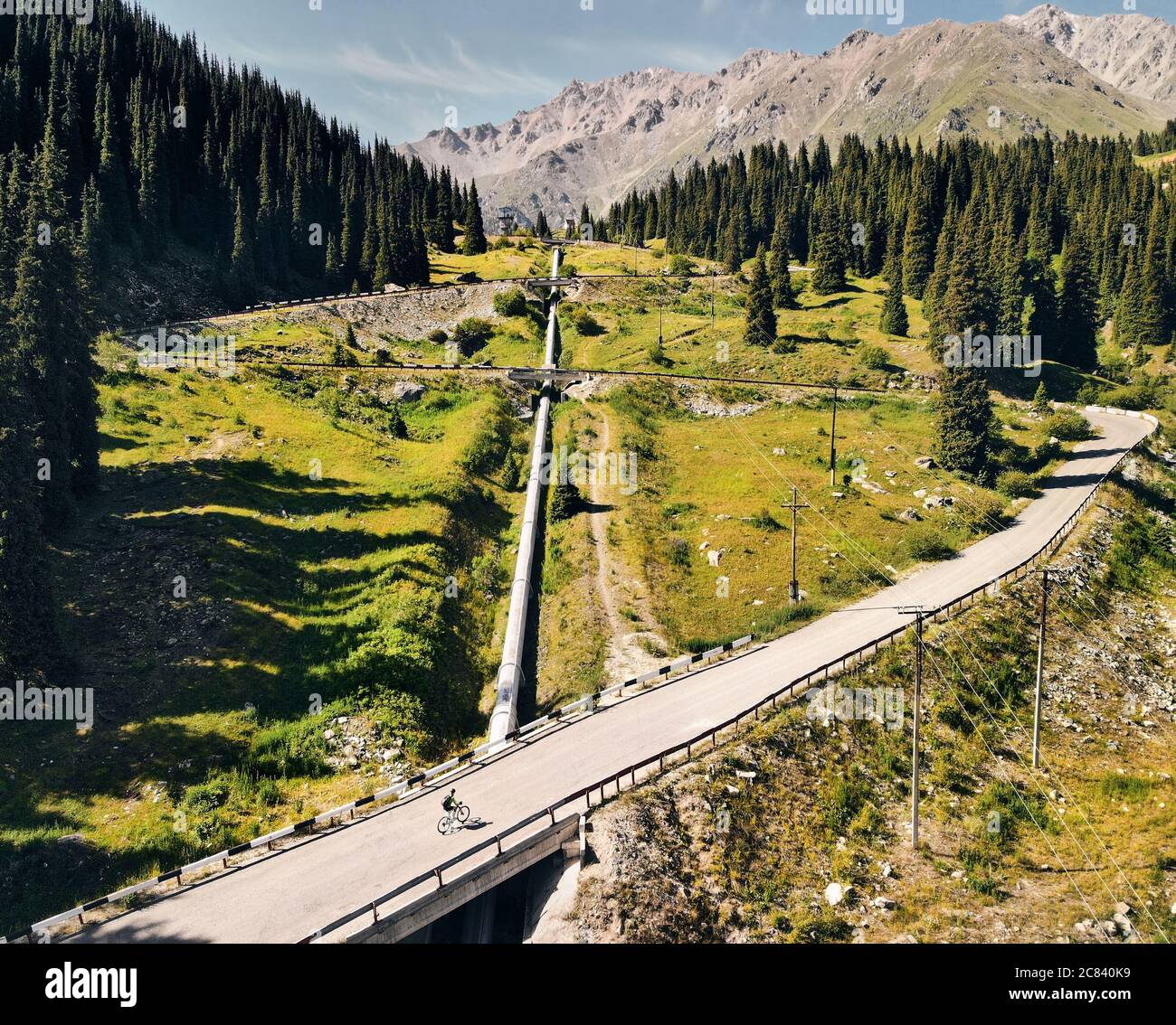 L'uomo in mountain bike corre sulla strada per la valle di montagna contro il cielo blu nuvoloso. Concetto di ricreazione e stile di vita sano Foto Stock