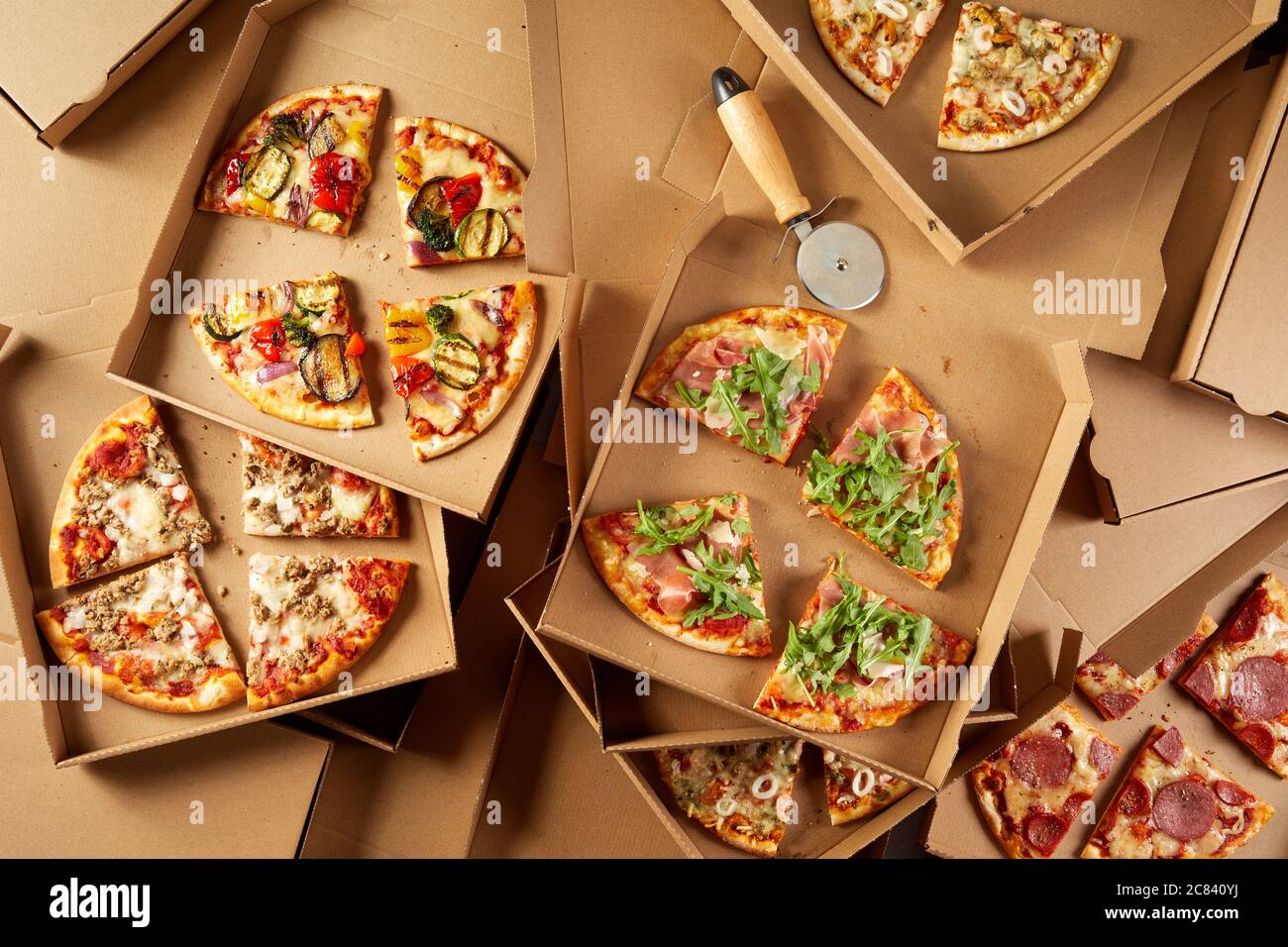 Vasto assortimento di condimenti su pizze italiane in scatole da asporto di cartone singole, viste dall'alto in basso, tagliate a porzioni con una taglierina per pasticceria Foto Stock