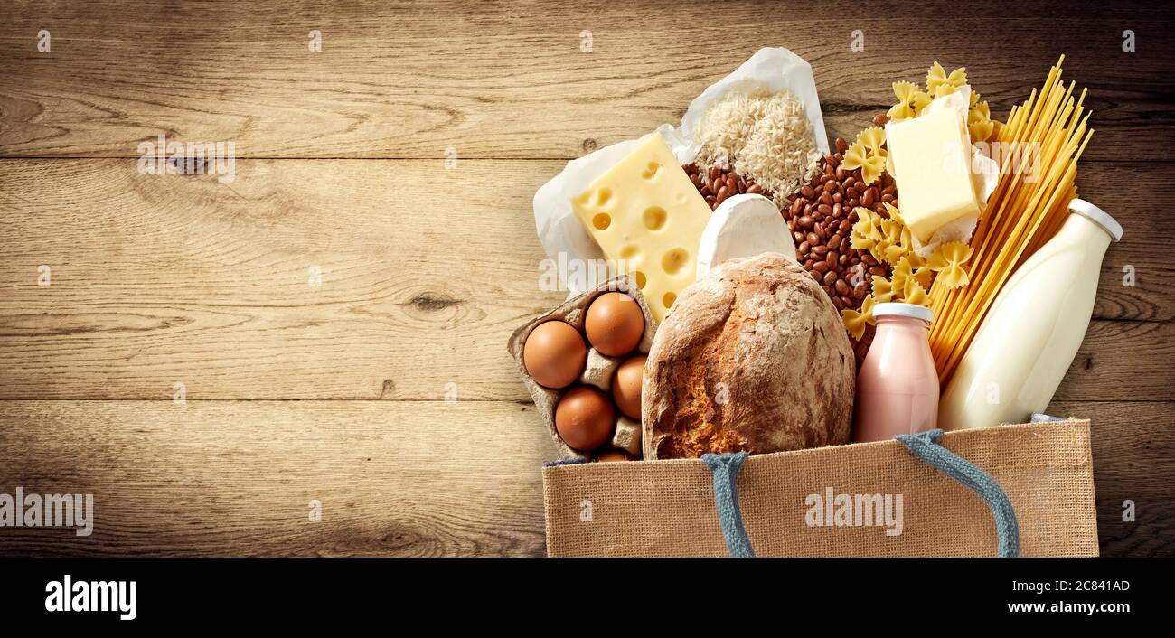 Generi alimentari freschi e latticini in una borsa riutilizzabile che comprende formaggio, pasta, baguette, fagioli, uova e latte su legno con copyspace e visco Foto Stock