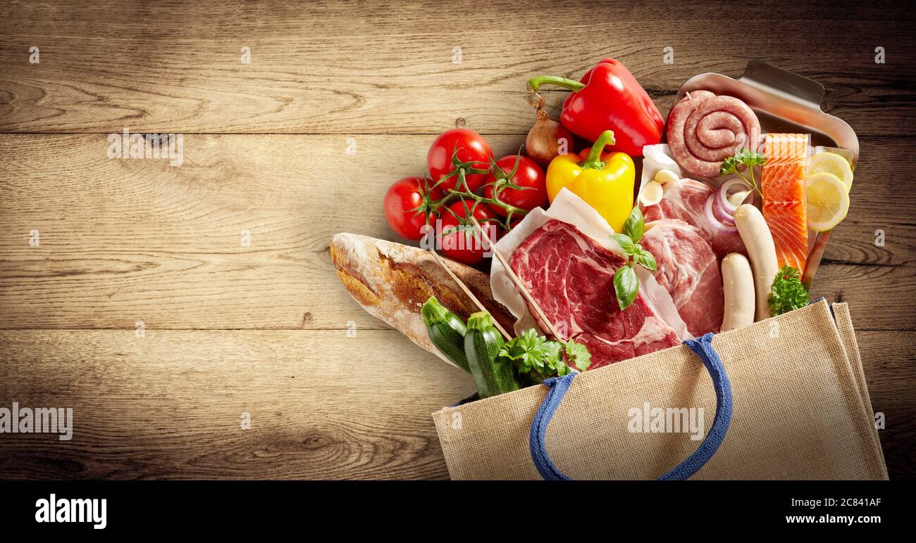 Panorama di carne assortita, pesce e prodotti freschi in una borsa della spesa che si spillano su uno sfondo di legno con vignette e copyspace in un sano dado Foto Stock