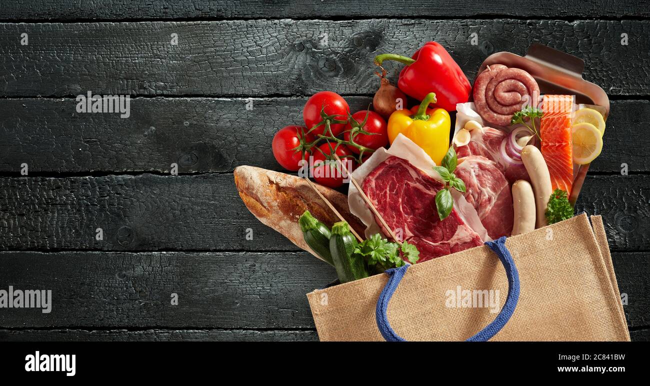 Borsa riutilizzabile piena di generi alimentari freschi, tra cui carne assortita, pesce, baguette, pomodori, peperoni dolci ed erbe in una vita still-lay piatta Foto Stock