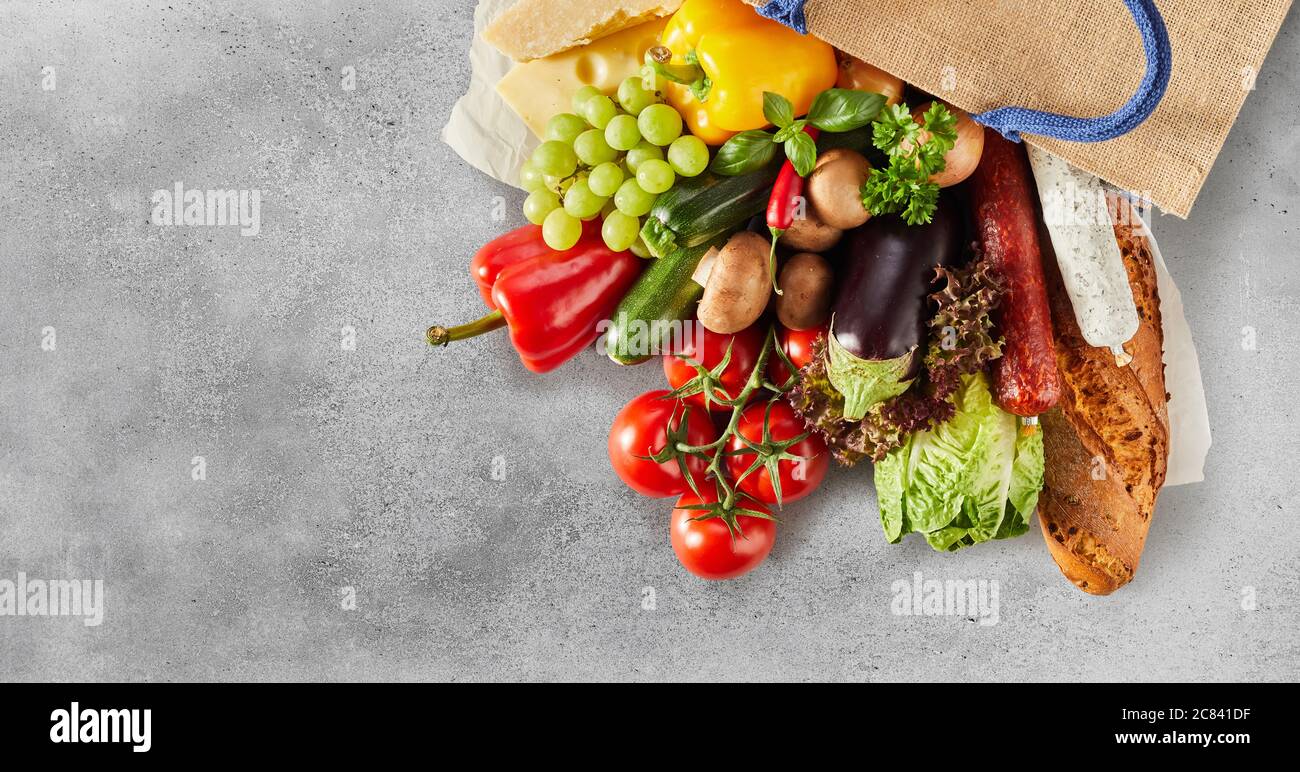 Verdure fresche, salumi, erbe e uva in una borsa riutilizzabile in una piatta still life su uno sfondo grigio testurizzato con copyspace in una padella Foto Stock