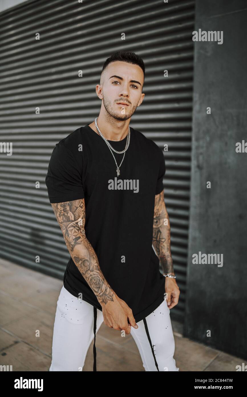 Anca europea tatuata maschio in una camicia nera e jeans strappati bianchi,  e catena in metallo Foto stock - Alamy