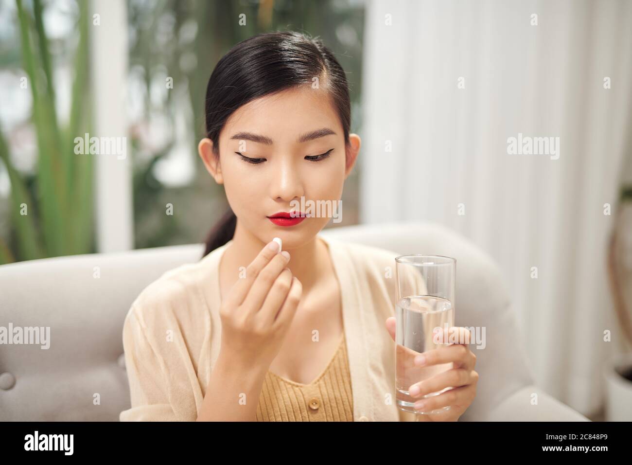 donna asiatica mangiare pillole di medicina per aumentare l'immunità con l'acqua e sentirsi meglio a casa Foto Stock