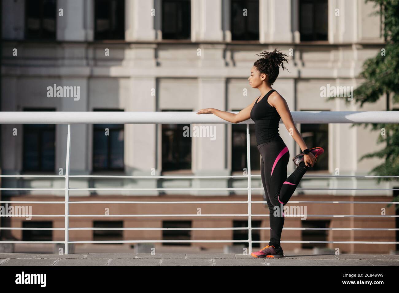 Atleta donna che si prepara per correre in città strada. Ragazza afroamericana in abbigliamento sportivo facendo scaldare i muscoli delle gambe nello stadio al mattino Foto Stock