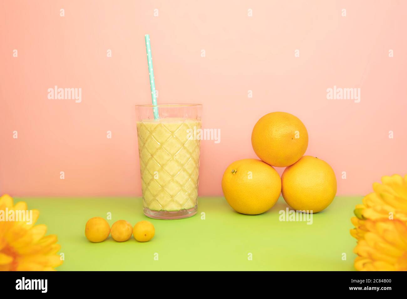 Cocktail estivo di frutta in stile retrò. Agitare nel bicchiere con paglia, arrangiamento di frutta arancione, fiori, sfondo rosa e verde. Foto Stock