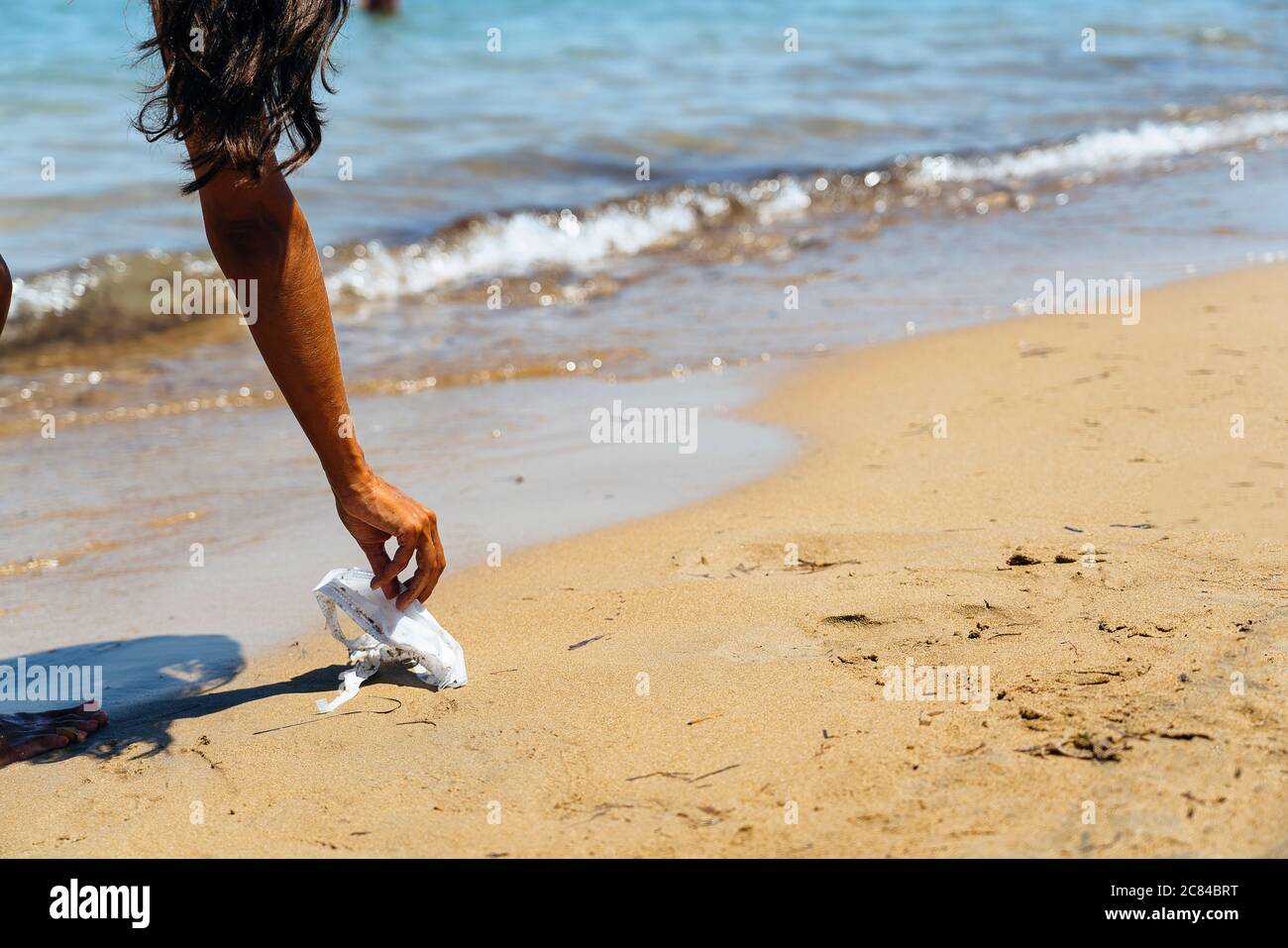 Donna che raccoglie i rifiuti in spiaggia, maschera facciale covid Foto Stock