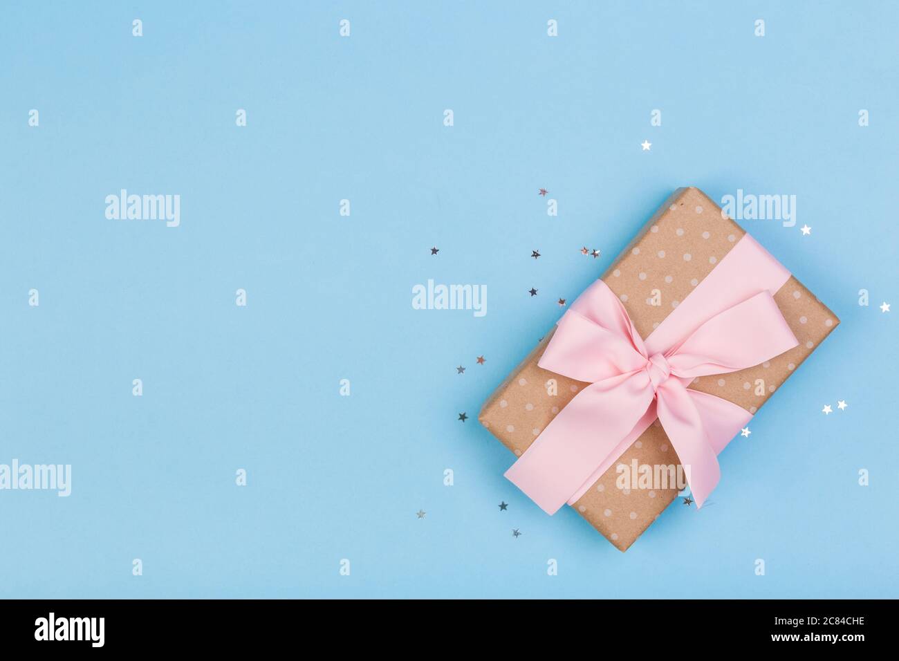 Confezione regalo o regalo e stelle confetti su un tavolo blu dall'alto. Composizione piatta per compleanno, giorno delle madri o matrimonio. Foto Stock