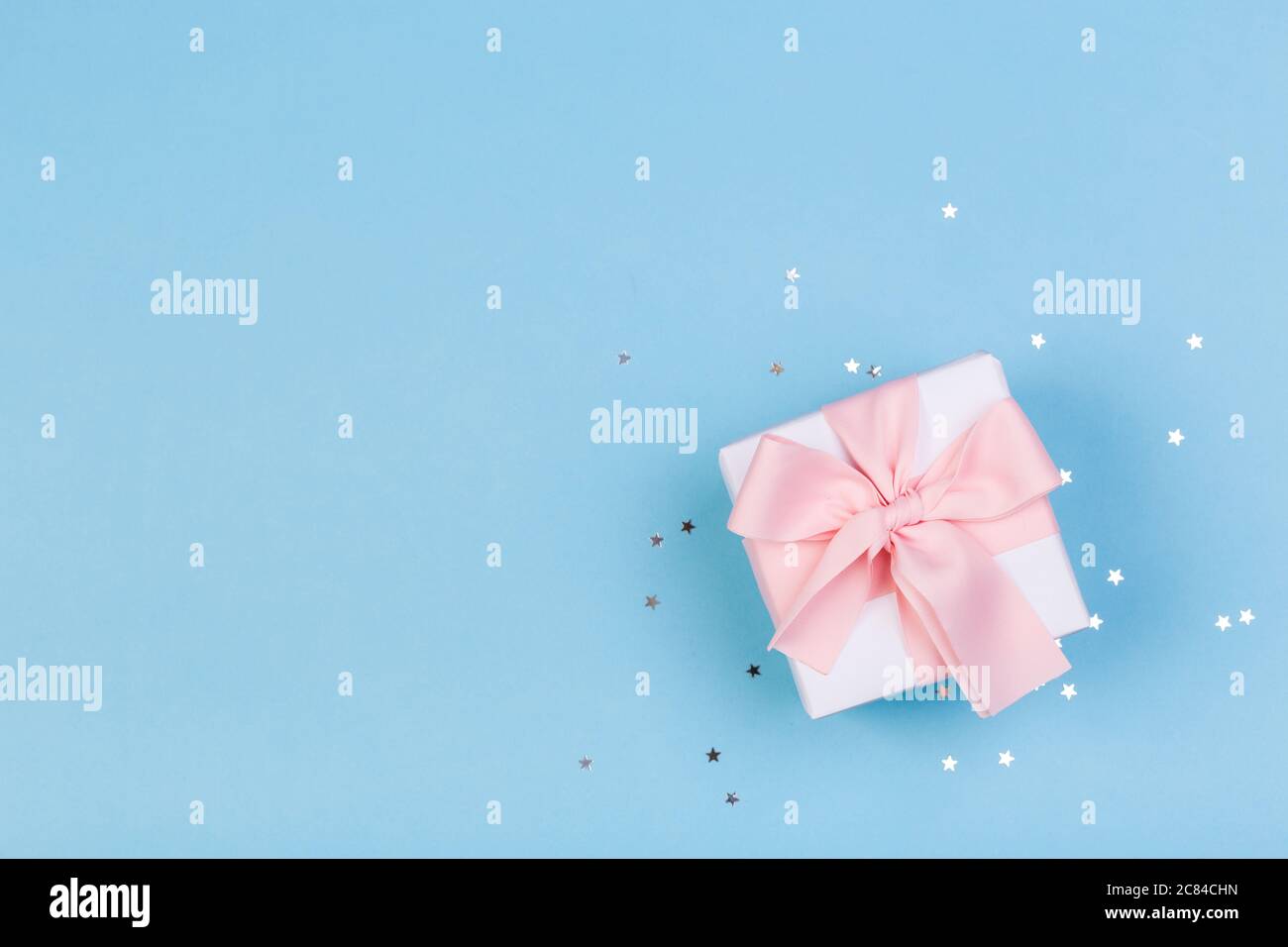 Confezione regalo o regalo e stelle confetti su un tavolo blu dall'alto. Composizione piatta per compleanno, giorno delle madri o matrimonio. Foto Stock