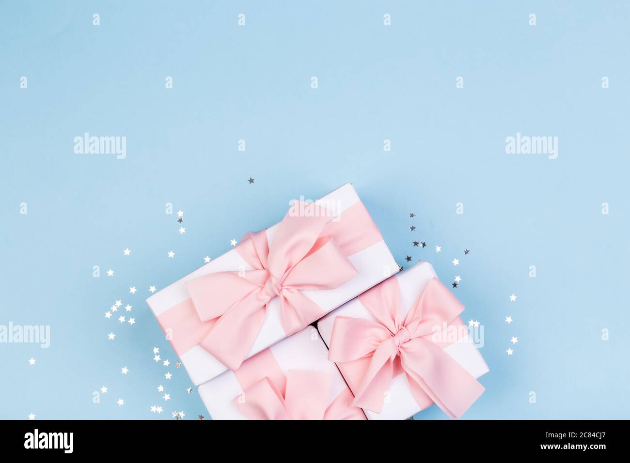 Confezione regalo o regalo e stelle confetti su un tavolo blu dall'alto. Composizione piatta per compleanno, giorno delle madri o matrimonio. Foto Stock