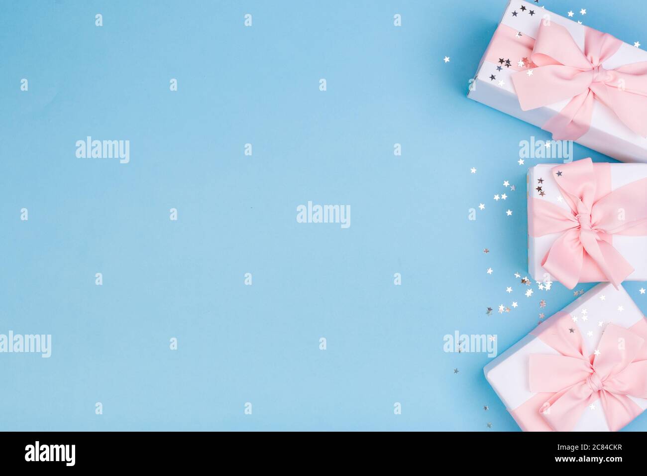 Confezione regalo o regalo e stelle confetti su un tavolo blu dall'alto. Composizione piatta per compleanno, giorno delle madri o matrimonio. Foto Stock