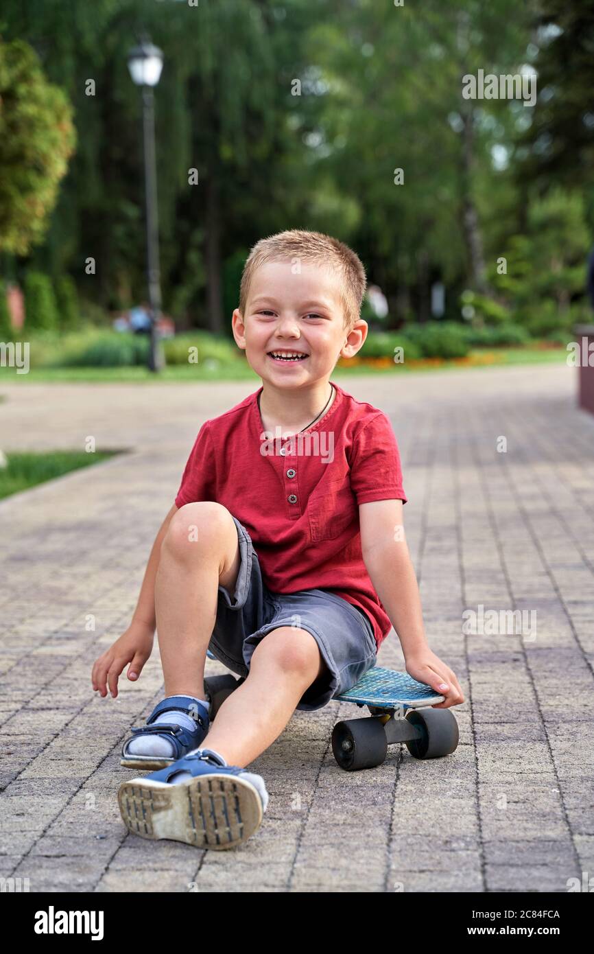 un ragazzino si siede su uno skateboard e ride Foto Stock