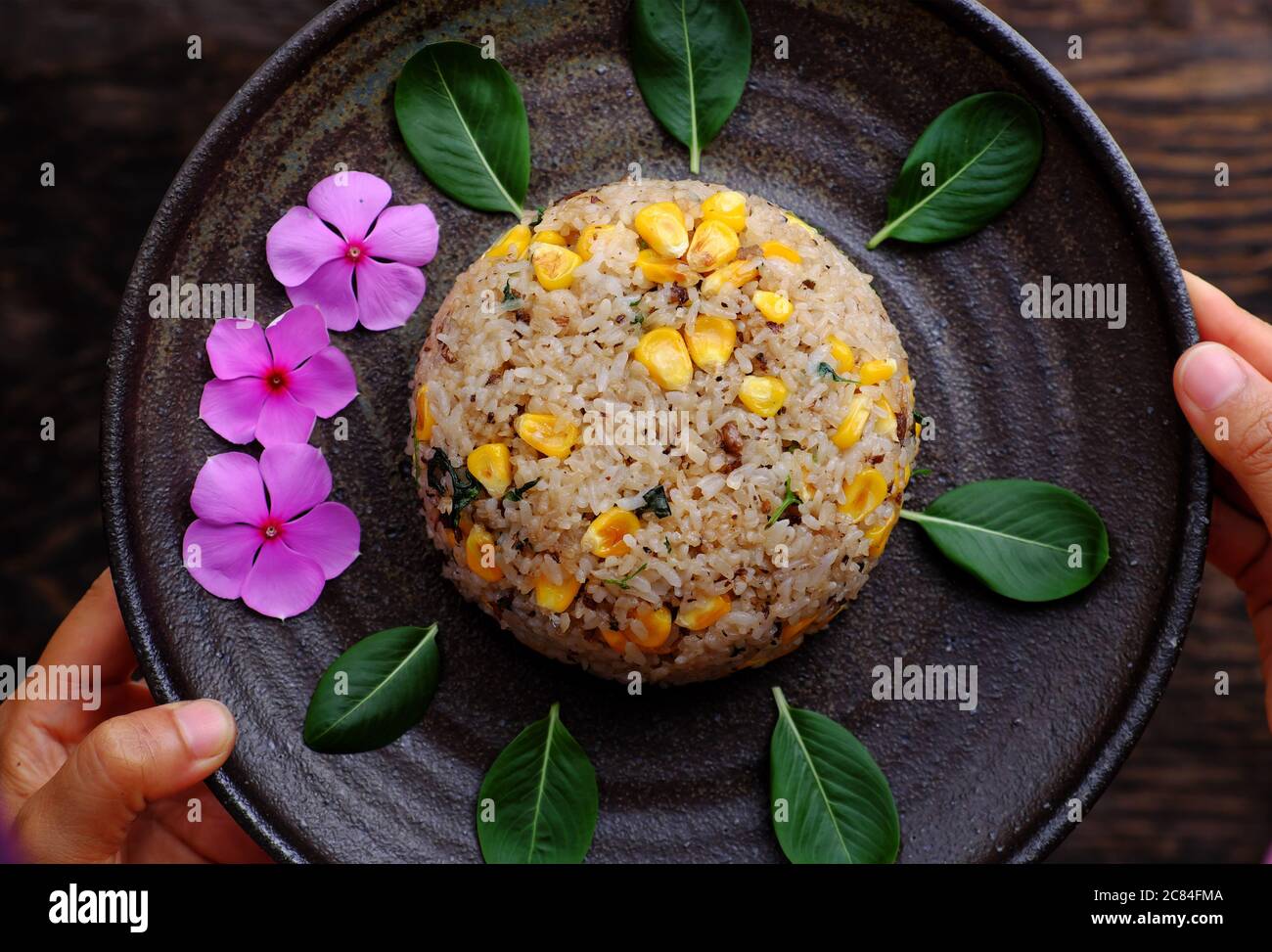Piatto vista dall'alto di riso fritto vegano vietnamita con mais giallo su sfondo scuro, donna tenere a mano deliziosi piatti vegetariani fatti in casa pronti a mangiare Foto Stock