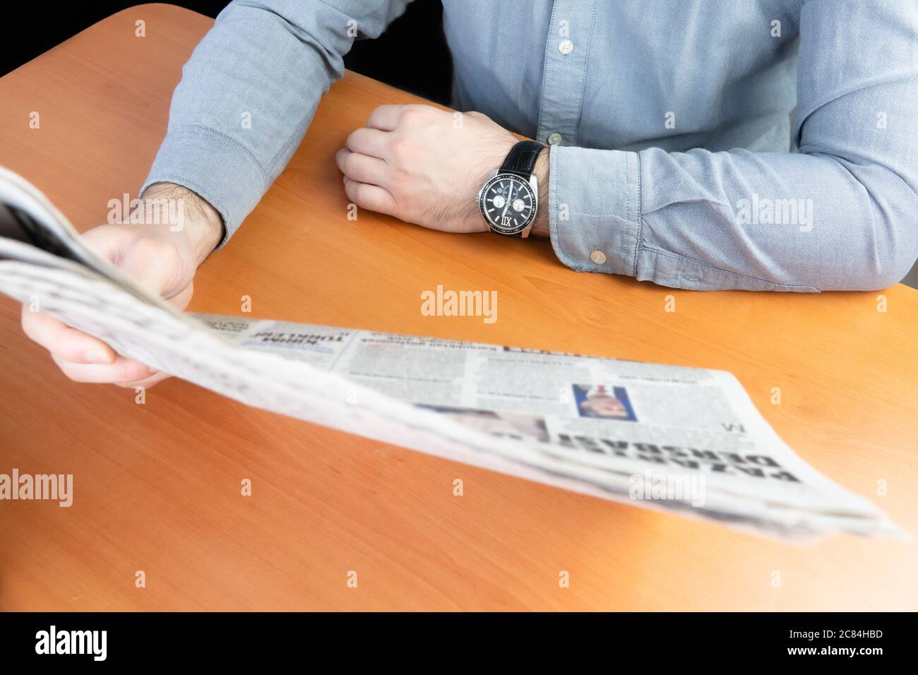 Uomo in camicia grigia leggendo giornale sul tavolo marrone Foto Stock