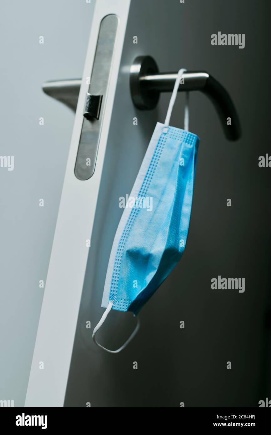 chiusura di una maschera chirurgica blu appesa al moderno pomello di una porta aperta Foto Stock
