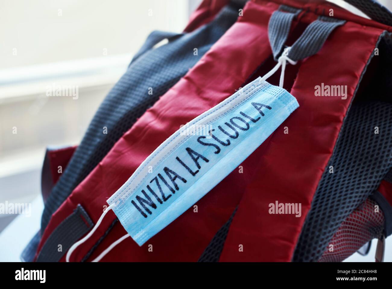 chiusura di una libreria rossa e grigia e di una maschera chirurgica blu con il testo di ritorno a scuola scritto in italiano, che raffigura la necessità di prevenire l'infettio Foto Stock