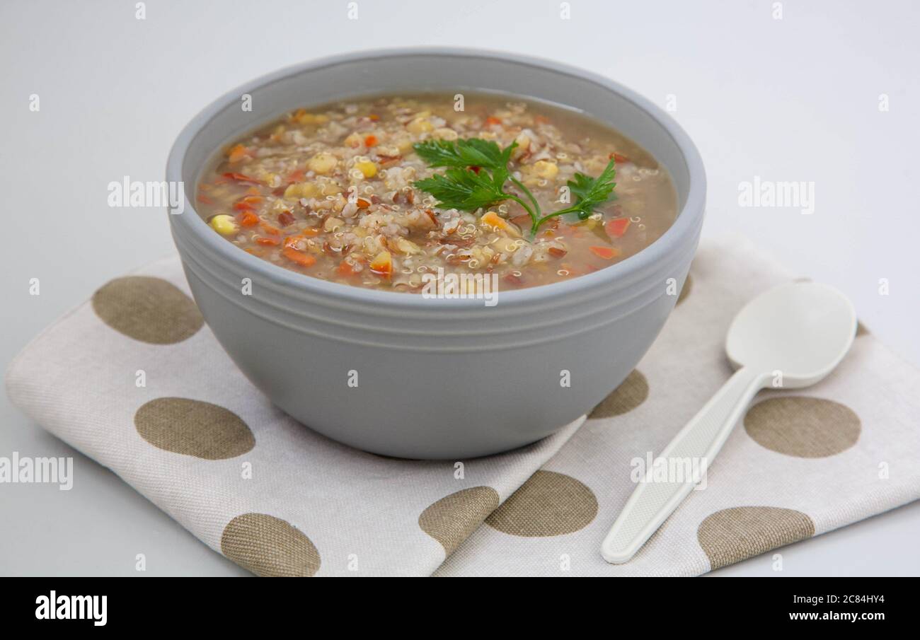 Zuppa di quinoa peruviana con riso rosso e lenticchie in una ciotola di argilla grigia guarnita con una foglia di prezzemolo verde Foto Stock