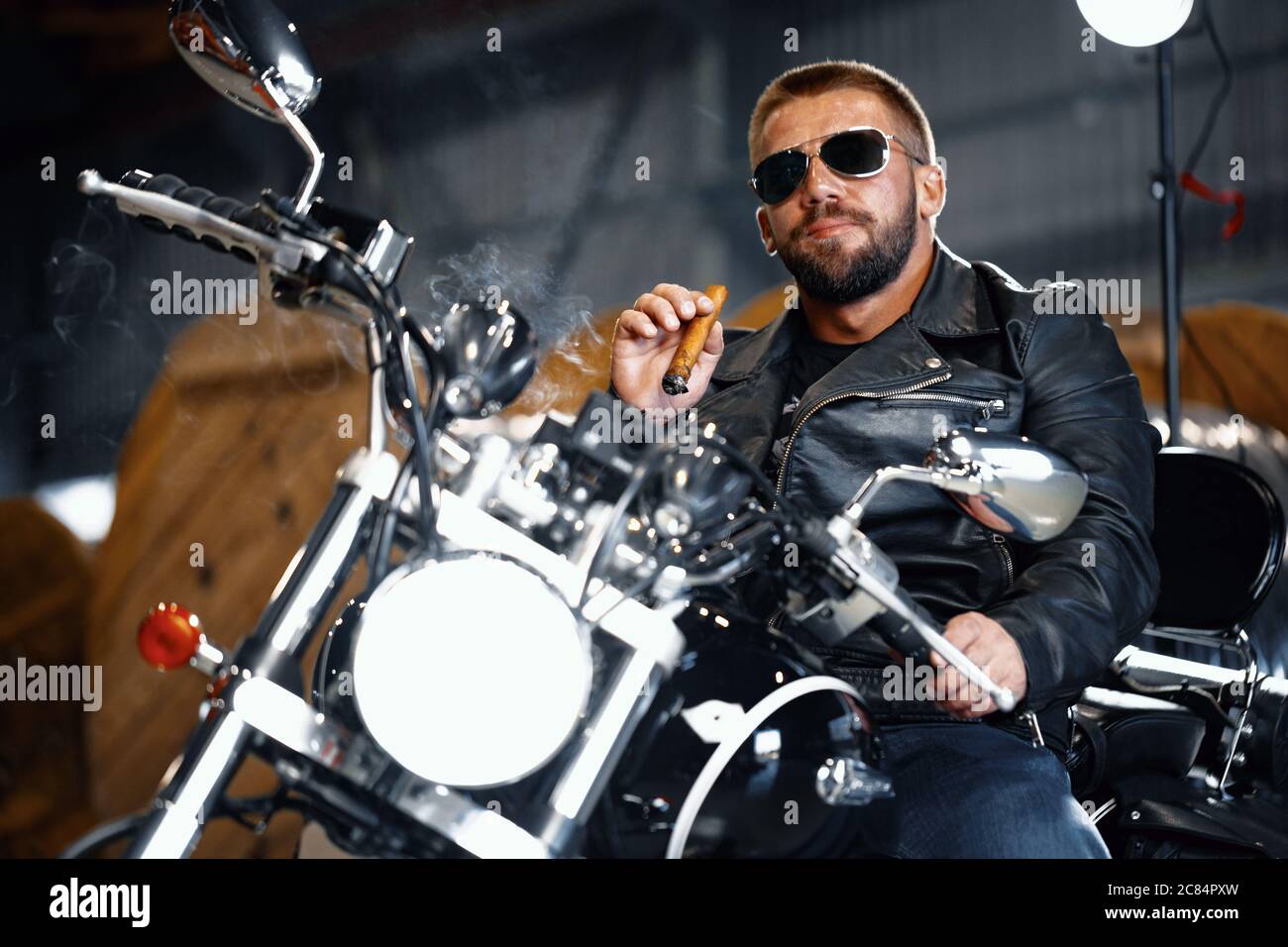 Biker uomo con bearded fresco in occhiali da sole seduti sulla sua moto e  fumare sigaro Foto stock - Alamy