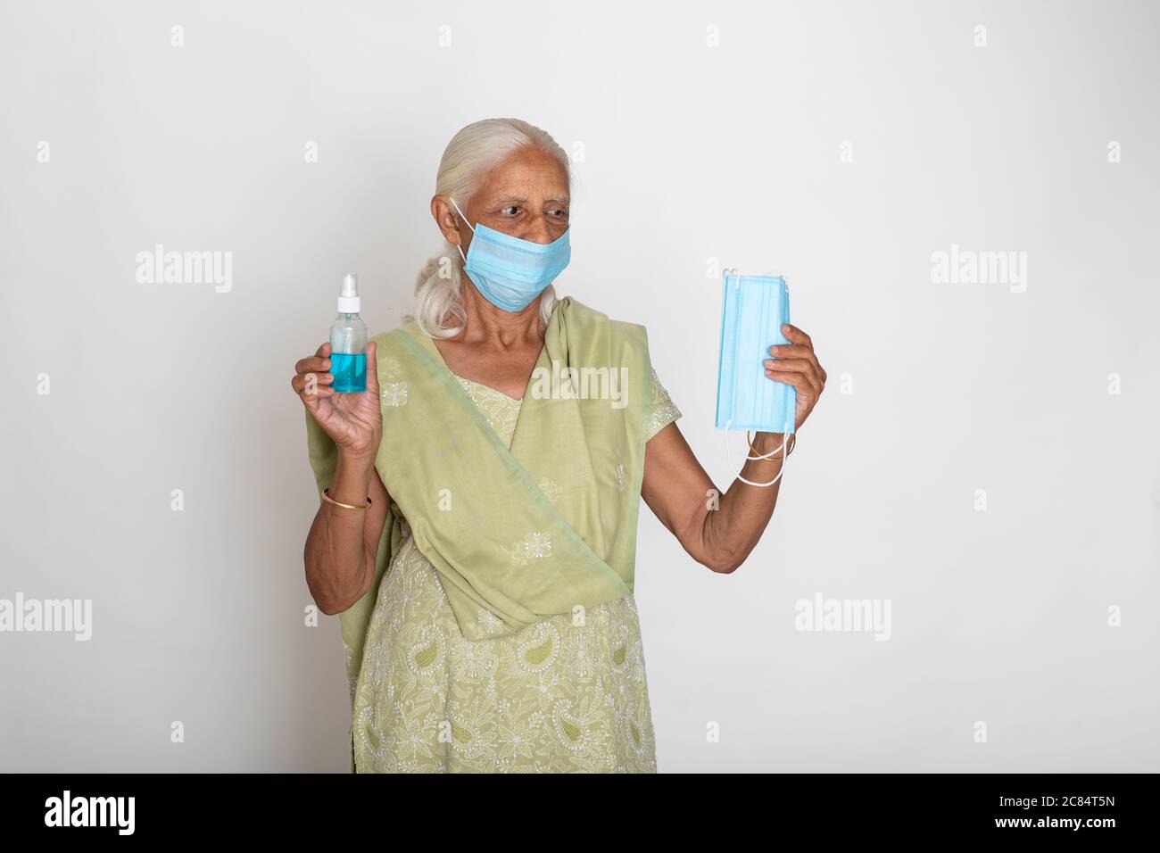 Donna indiana matura che indossa maschera di protezione Covid, nonna indiana mostra maschera di protezione viso e disinfettante Foto Stock