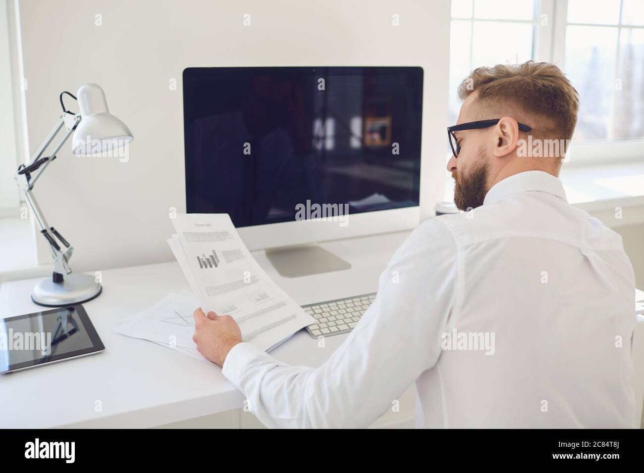 Un uomo d'affari lavora a un tavolo con un computer in ufficio. Vista posteriore. Foto Stock