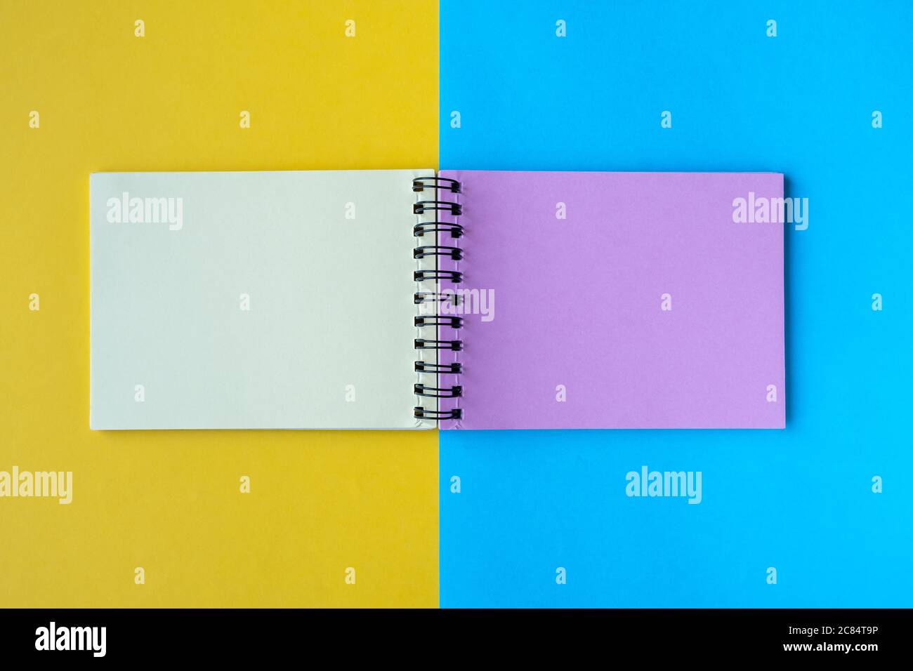 Un notebook con pagine multicolore si trova su uno sfondo giallo e blu. Vista dall'alto, disposizione piatta, spazio per il testo. Foto Stock