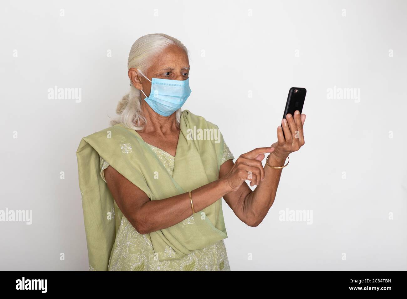 Donna indiana matura che indossa maschera di protezione Covid, nonna indiana controlla il suo telefono cellulare Foto Stock