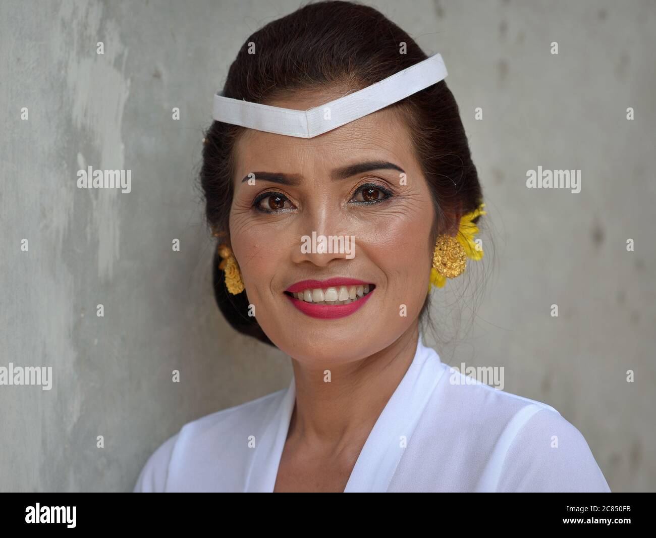 La donna balinese indonesiana matura indossa abiti bianchi e sorrisi per la macchina fotografica durante una cerimonia religiosa indù tempio (Odalan festival). Foto Stock