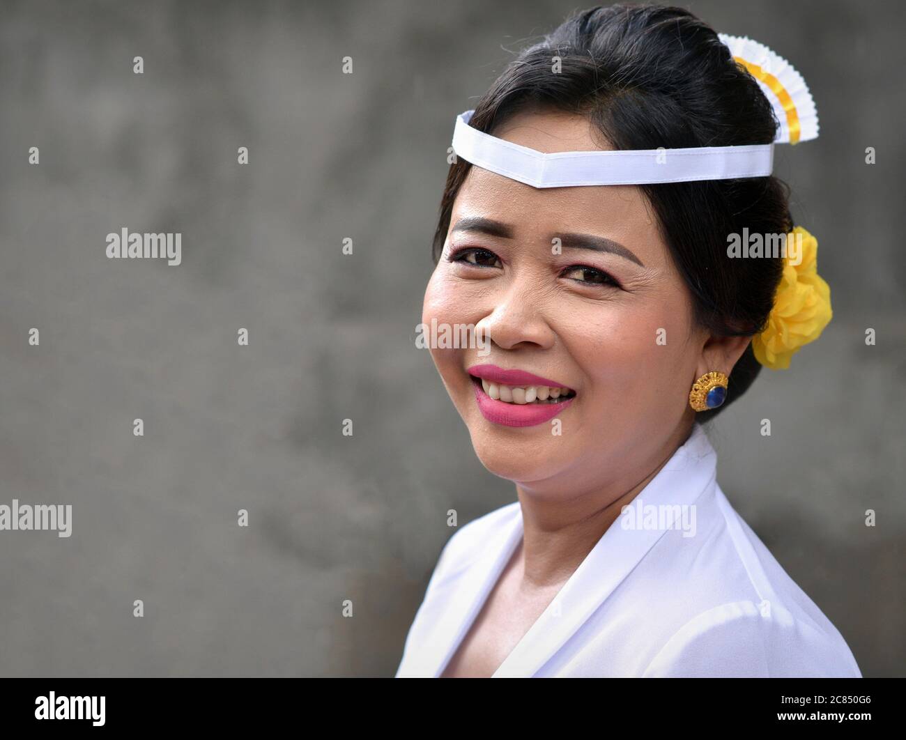 La donna balinese indonesiana matura indossa abiti bianchi e sorride per la macchina fotografica durante una cerimonia religiosa indù tempio (Odalan festival). Foto Stock
