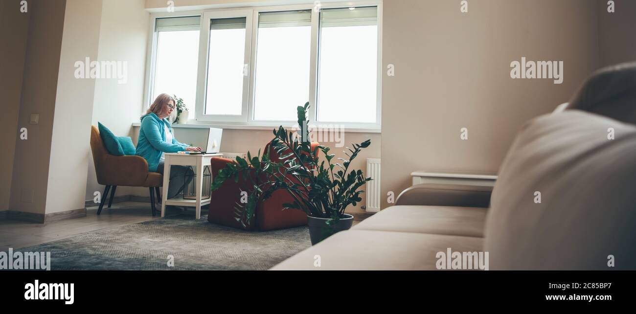 Bionda donna anziana che lavora a distanza da casa sul laptop durante il blocco Foto Stock