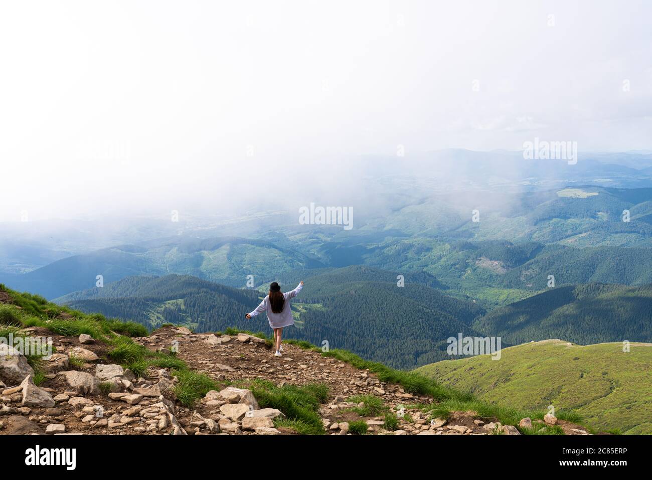 La ragazza si erge sulla cima della montagna e gode della vista sulla valle. All'alba, mani in su Foto Stock