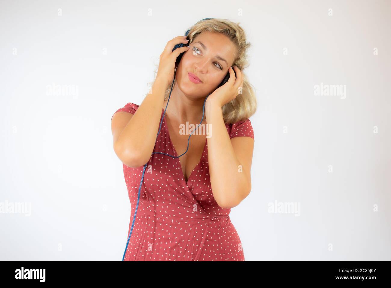 Bella donna bionda sorridente in abito rosso con cuffie Foto Stock