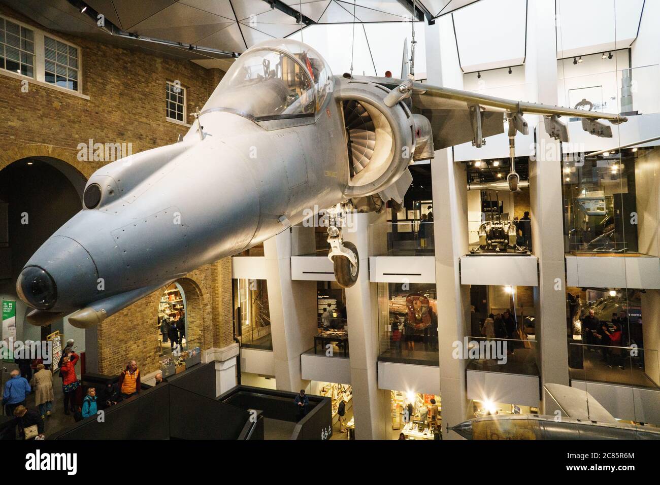 Harrier Jump Jet Imperial War Museum Londra // LONDRA, Regno Unito — Un Harrier Jump Jet è sospeso sopra la sala principale dell'Imperial War Museum di Londra. L'iconico aereo di fabbricazione britannica, noto per le sue capacità di decollo e atterraggio verticali, funge da fulcro della vasta collezione di manufatti militari del museo e mostre incentrate sulla guerra moderna e sul suo impatto sulla società. Foto Stock