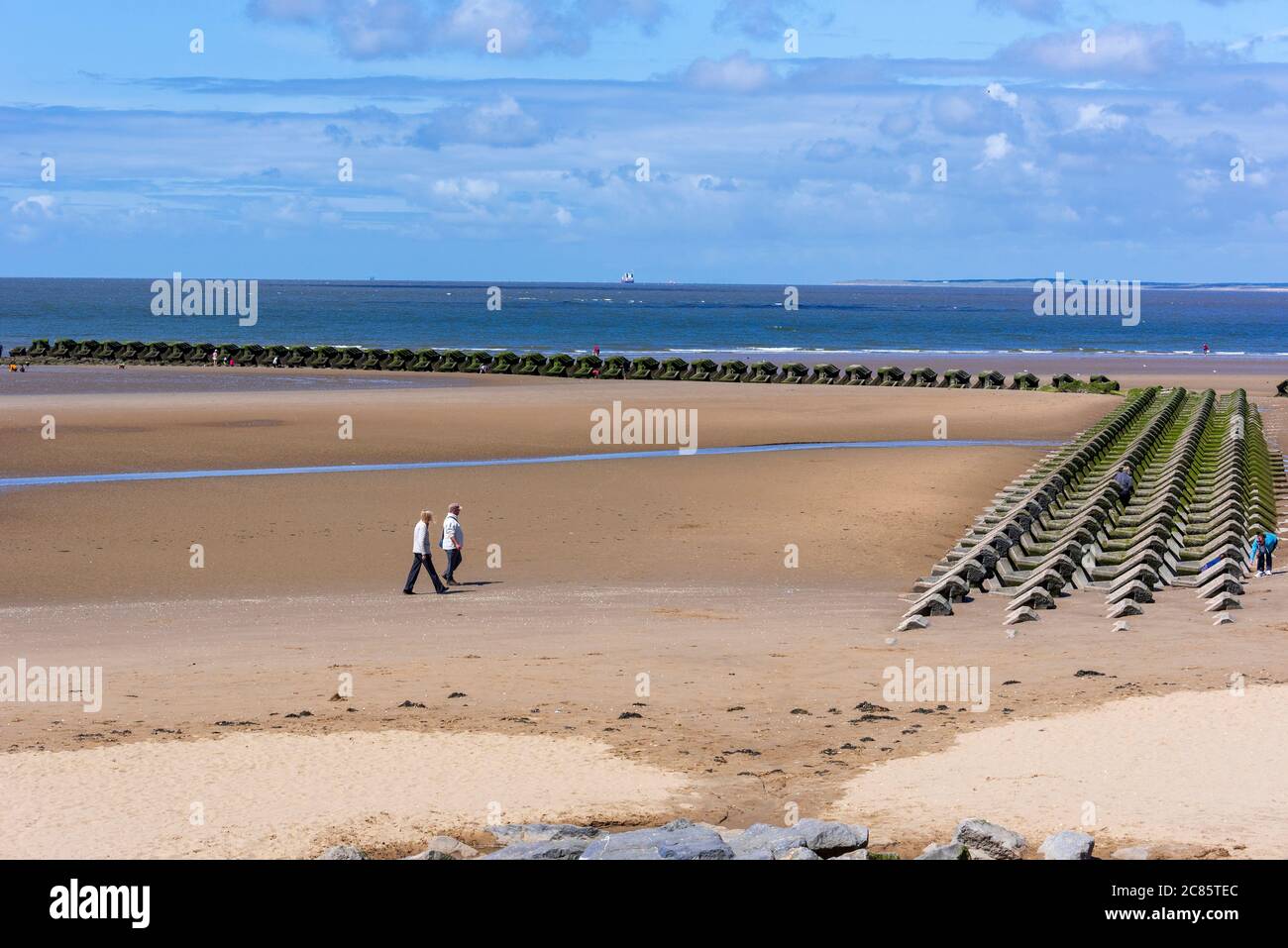 Le persone che passeggiano sulla spiaggia di New Brighton sul Wirral al sole accanto alle massicce difese marine in cemento. Foto Stock