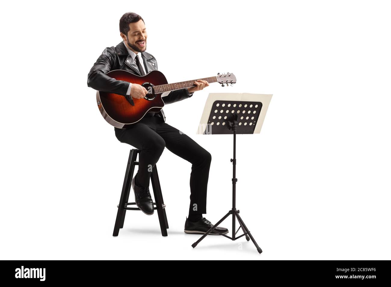 Musicista che suona una chitarra acustica e guarda un notebook musicale su uno stand isolato su sfondo bianco Foto Stock