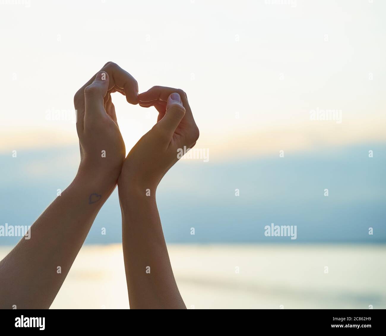 Mano femminile e maschile che mostra il cuore, simbolo dell'amore, sfondo della spiaggia Foto Stock