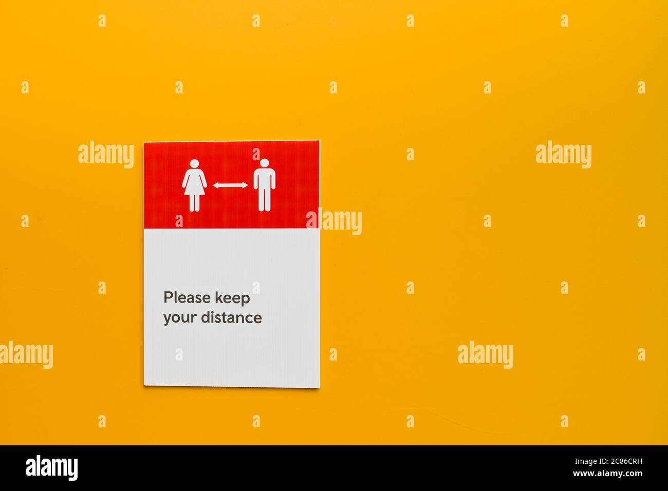 Avviso su un muro giallo semplice che chiede alla gente di mantenere la distanza sociale. Nessuna gente. Spazio di copia. Foto Stock