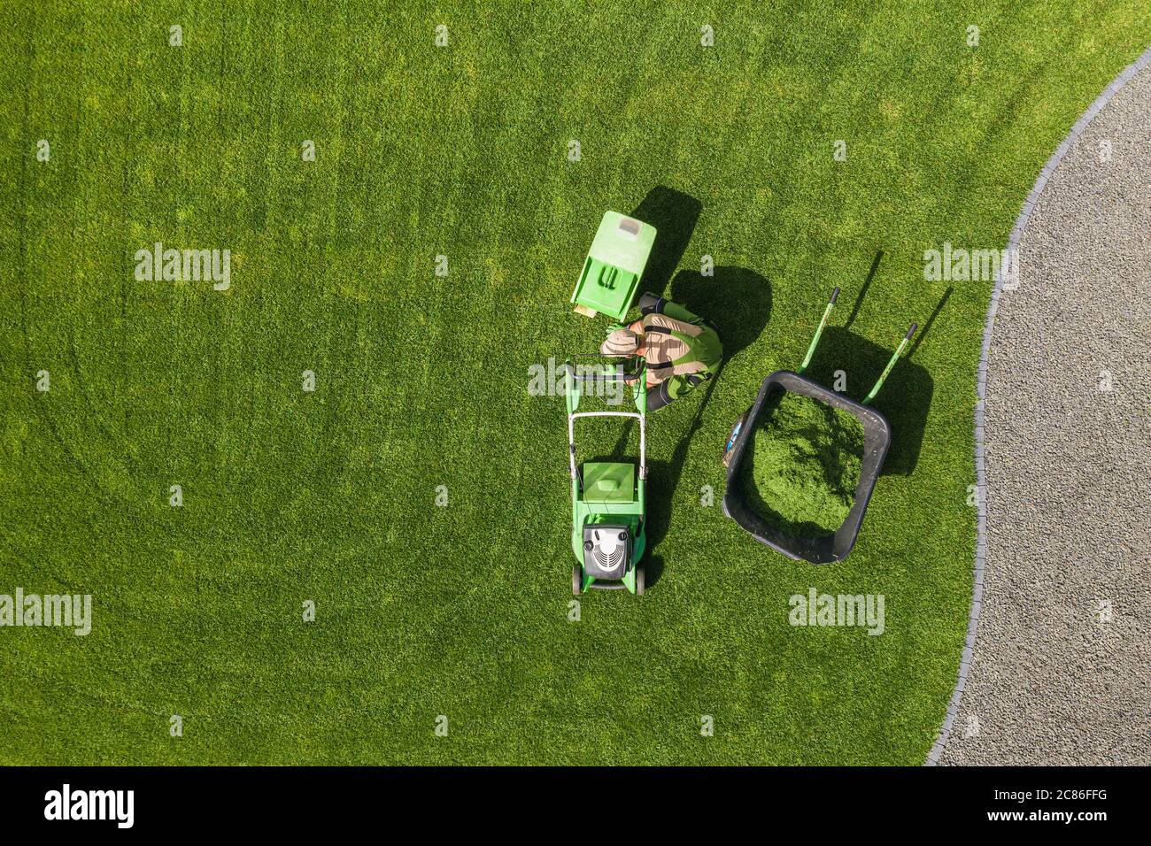 Vista aerea del cortile Giardino falciatura prato e manutenzione settimanale. Giardiniere caucasico nei suoi 40 anni con tosaerba moderno Rimozione di erba tagliata dal Fie Foto Stock