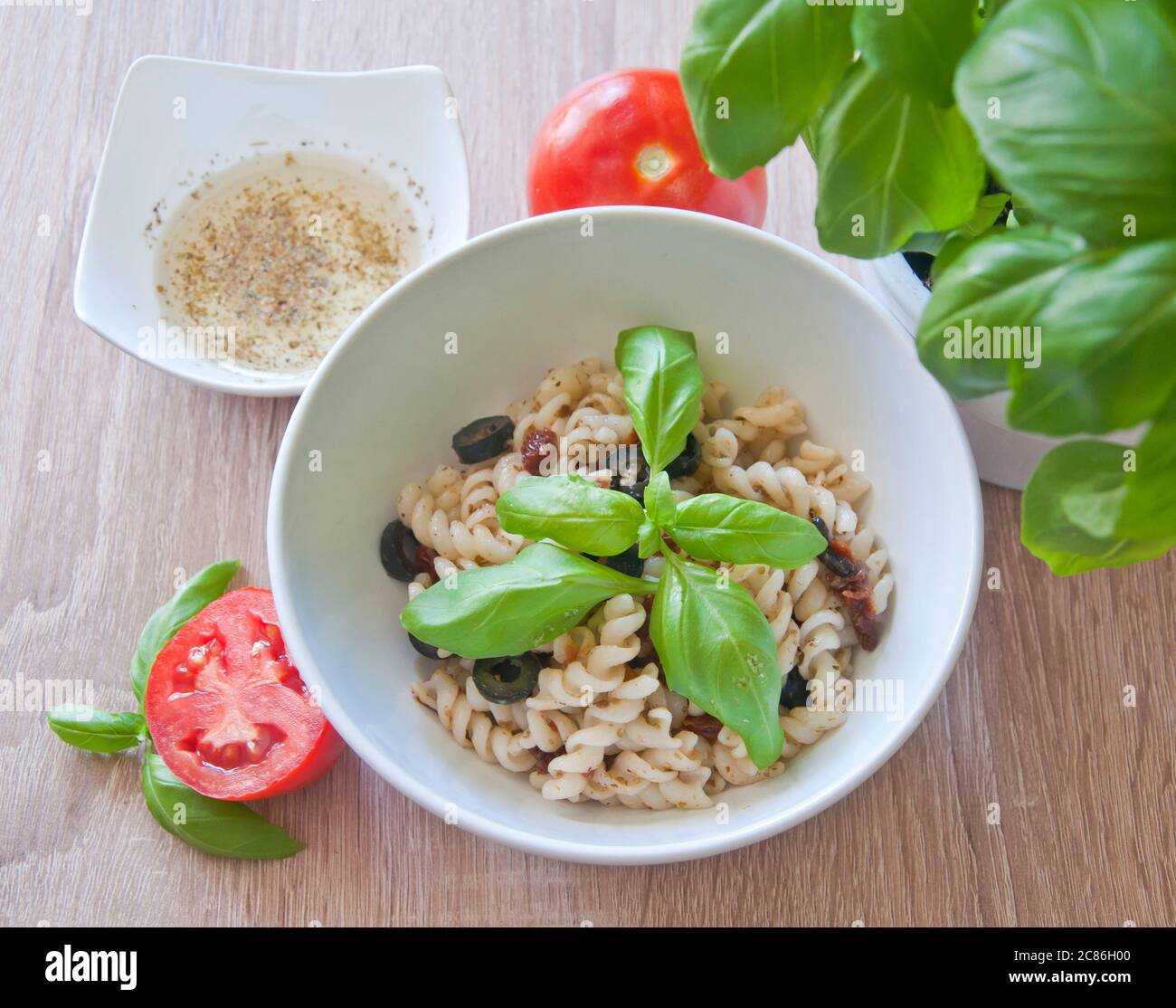 Gustosa pasta con olive, pomodori secchi e condimento alle erbe. Decorata con basilico e pomodori freschi su sfondo di legno. Pasto dietetico. Foto Stock