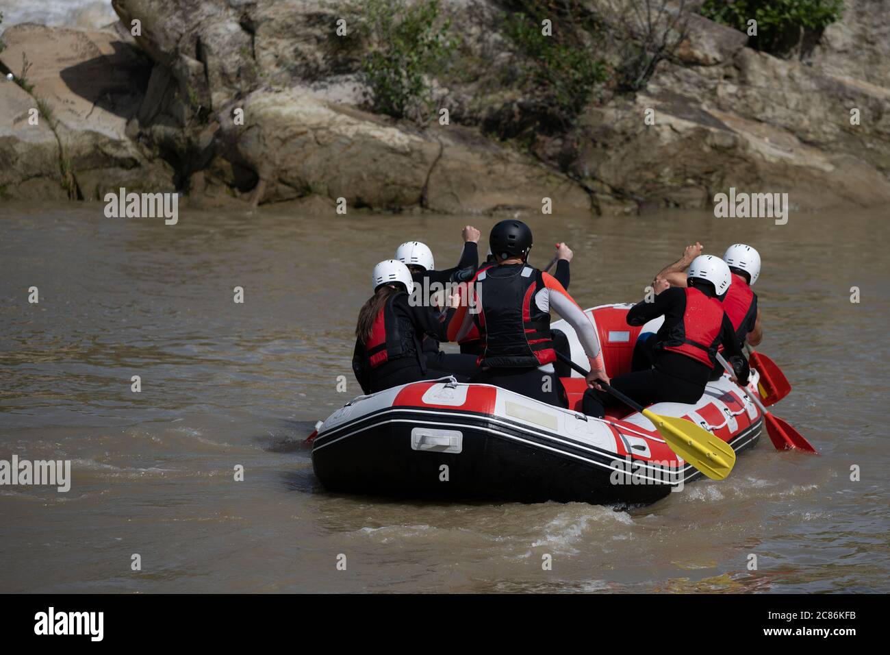 I membri della squadra che girovagano sulla barca da rafting lungo il fiume torbido durante l'estate. Attrezzatura completa con casco incluso Foto Stock