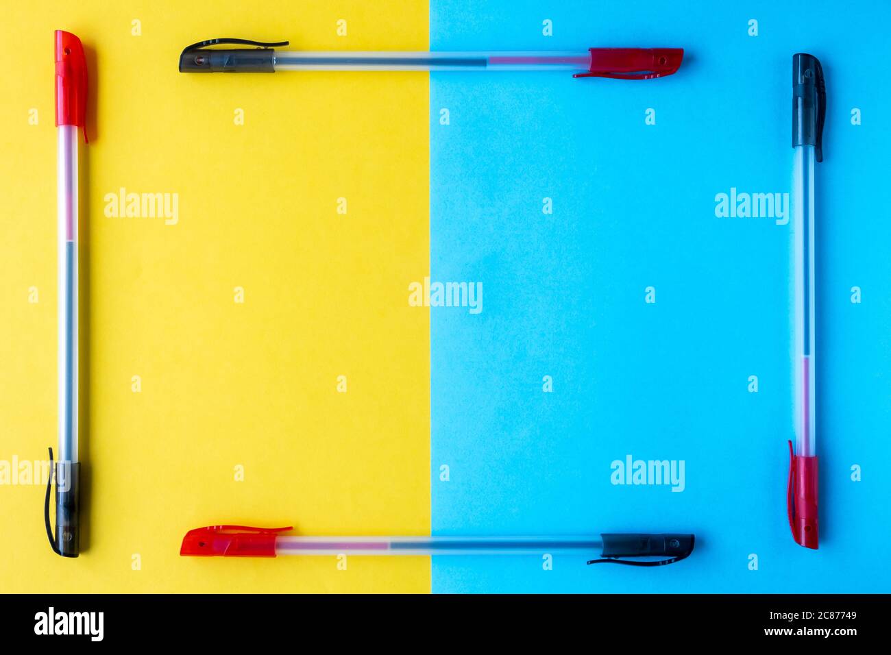 Una cornice di penne a sfera a due colori su sfondo giallo e blu. Disposizione piatta, spazio per il testo, vista dall'alto. Foto Stock