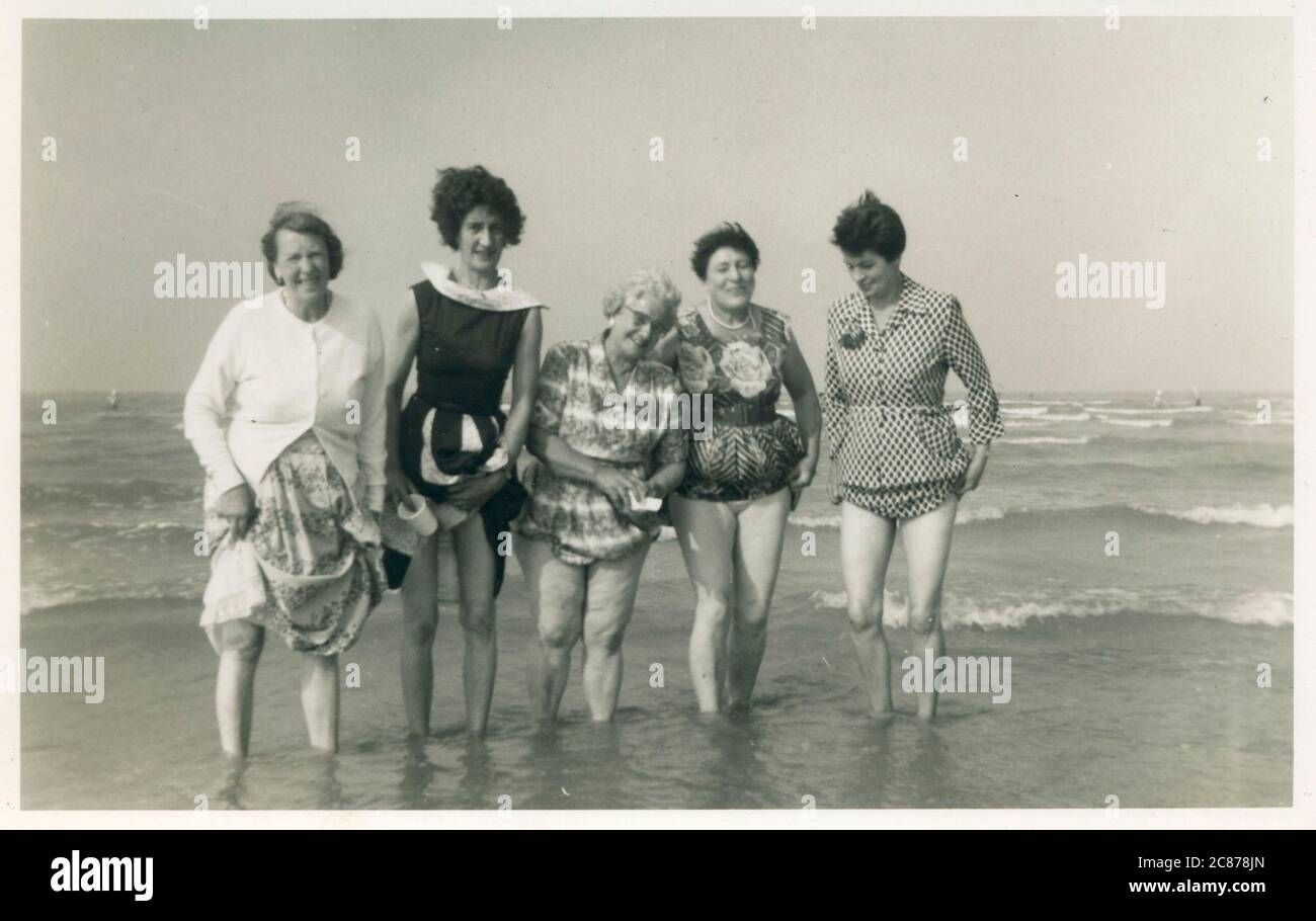 Cinque donne, di diverse età, forme e dimensioni, hanno fotografato pagaiando in mare in una giornata di blustery in spiaggia. Foto Stock