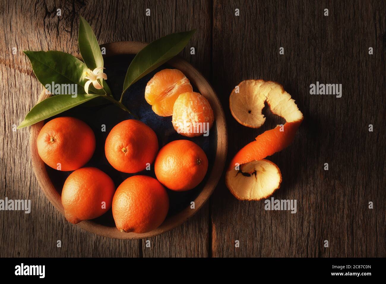 Primo piano della vita morta di Minneola Tangelos su un piatto con foglie e fiori d'arancio su un tavolo rustico in legno, e calda luce laterale. Foto Stock